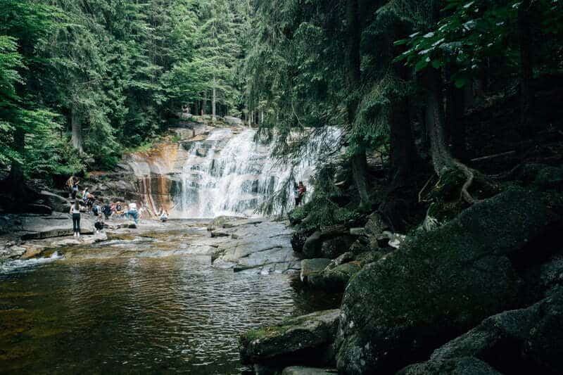 people enjoy the cool water from a forest lined waterfall